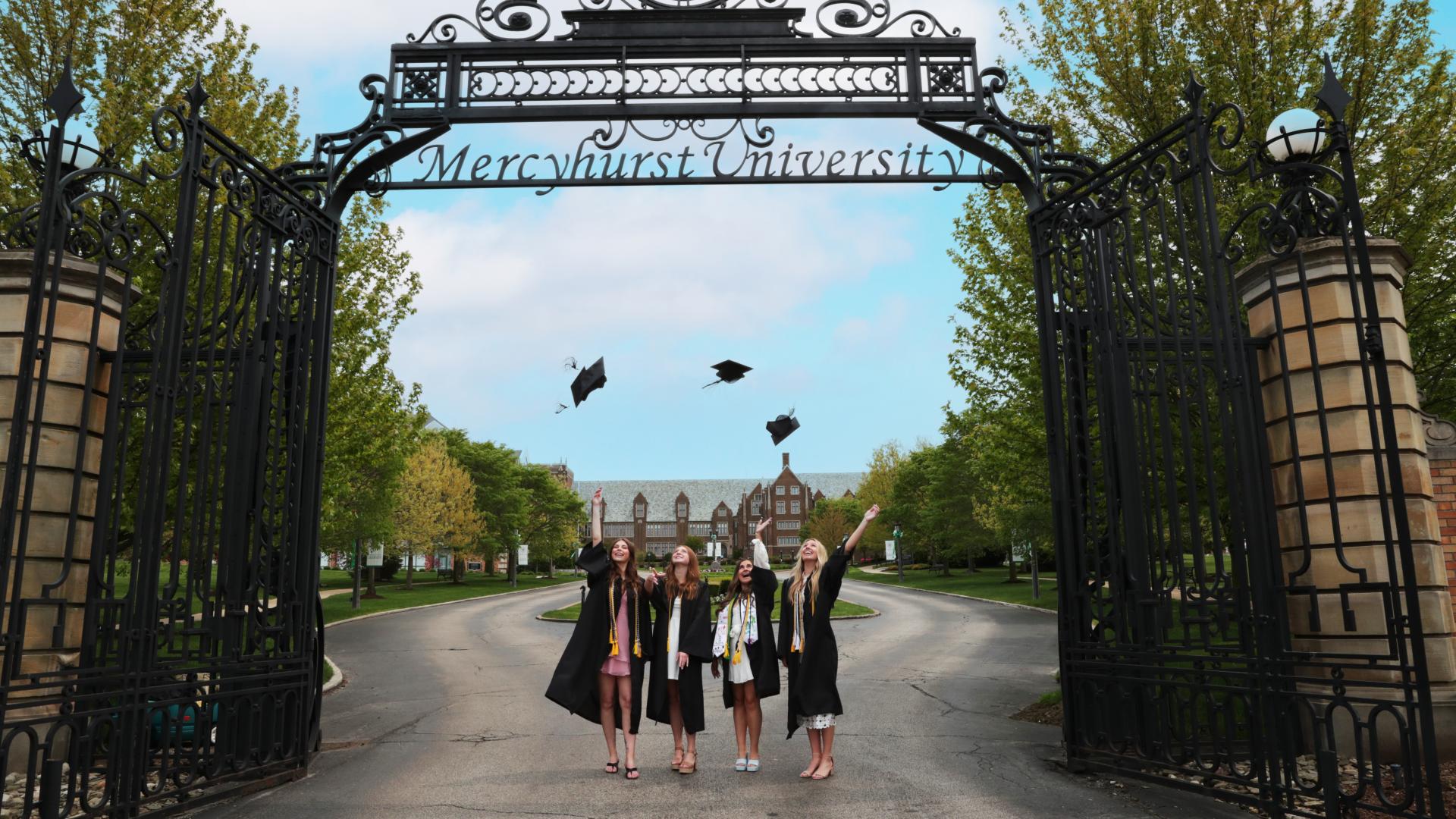 four female students throw graduation caps under the Ĳʿ gates